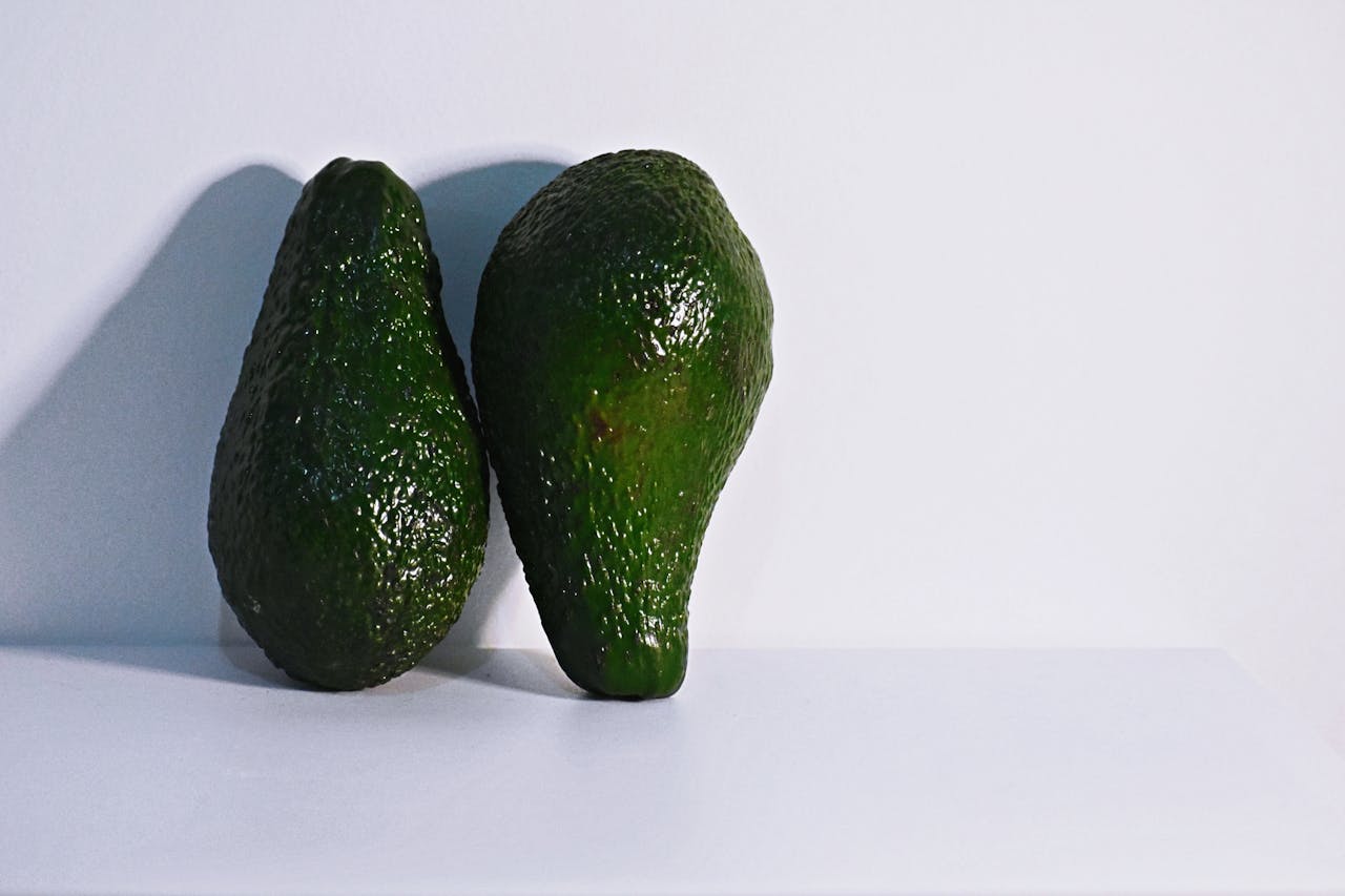 Two Green Avocados on White Surface